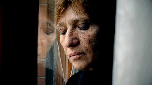 靠近悲伤和沮丧的成熟女人靠在窗户上