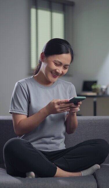 亚洲女性坐在家里的沙发上使用智能手机