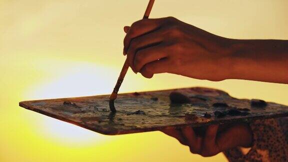一位年轻的女艺术家在明亮的日落时分在调色板上调色油画