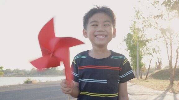 夏天的花园里幸福的小男孩在麦田里微笑手里拿着小风轮或风车玩具