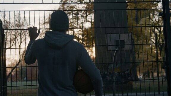 一个拿着球的男人看着空荡荡的篮球场