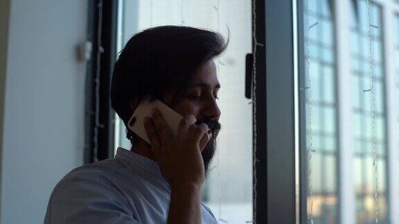 在现代办公室里一个乐观的印度商人站在窗边打电话