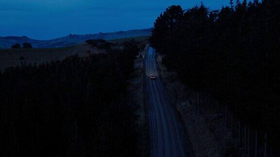 鸟瞰图汽车行驶在乡村道路上SUV驾驶在黄昏与前灯穿过松树