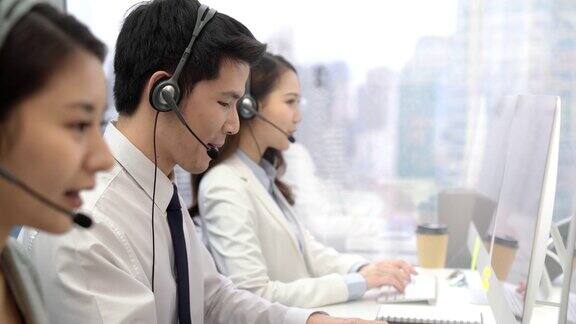 年轻的亚洲男性电话推销员与同事在呼叫中心城市办公室