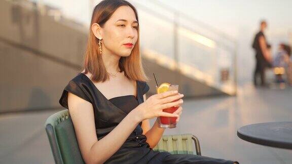 日落时分一名4K亚洲女子在摩天大楼的屋顶餐厅喝着鸡尾酒等朋友