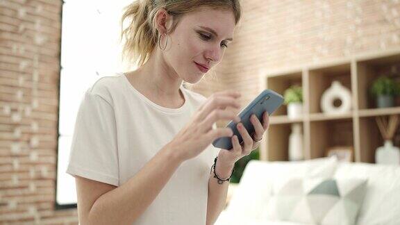 年轻的金发女子坐在卧室的床上使用智能手机