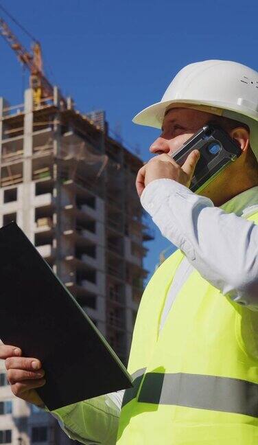 垂直:工头在施工现场检查计划和打电话