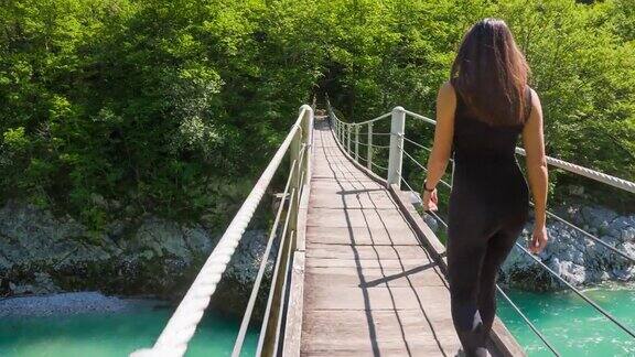 年轻的女性走在充满活力的山谷的木制吊桥上