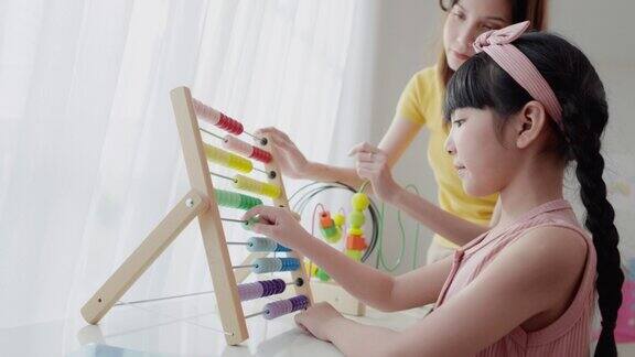 一位亚洲美女老师正在向她可爱的6岁亚洲女学生讲解如何使用彩色算盘进行计算她将计数器沿框中代表数字的杆子滑动数学教室