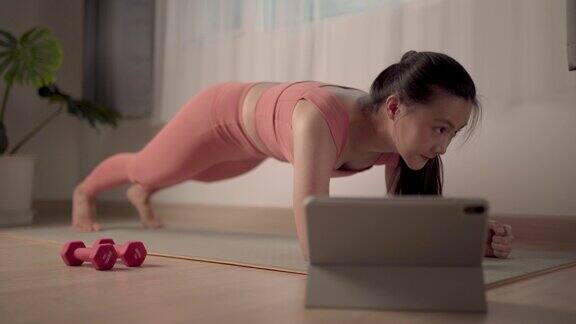 亚洲妇女穿着运动服装在家里的垫子上锻炼同时观看视频博客在线