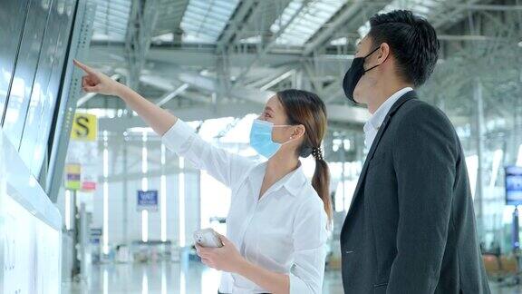 亚洲商务人士佩戴口罩在候机楼登机信息屏幕上查看地图和航班时刻表