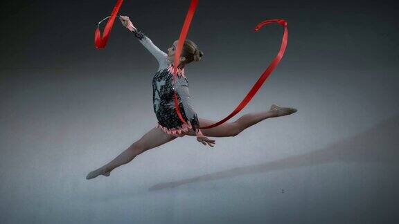 艺术体操运动员旋转她的红丝带并表演跳跃