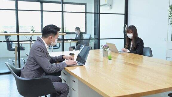 一群年轻的亚洲团队商务人士戴着口罩在办公室工作并在公司工作场所保持距离社交距离