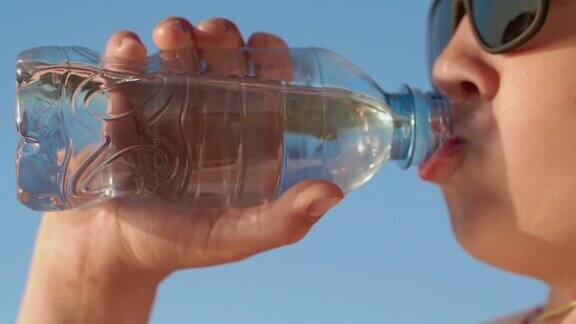 戴墨镜的男孩拧开水瓶的瓶塞喝水