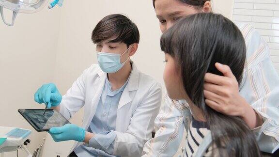 亚洲男性儿科牙医在牙科诊所向一个女孩解释牙齿x光片