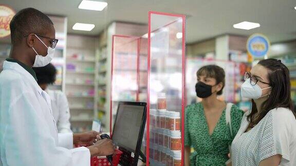 一名年轻的药剂师戴着口罩在药店为一名年轻女性看病