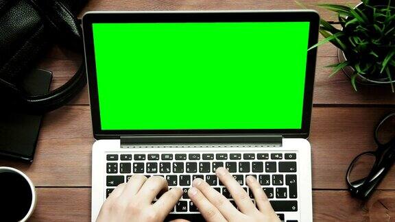 俯视图男性双手工作的笔记本电脑与绿色屏幕在白色的桌子上从上方