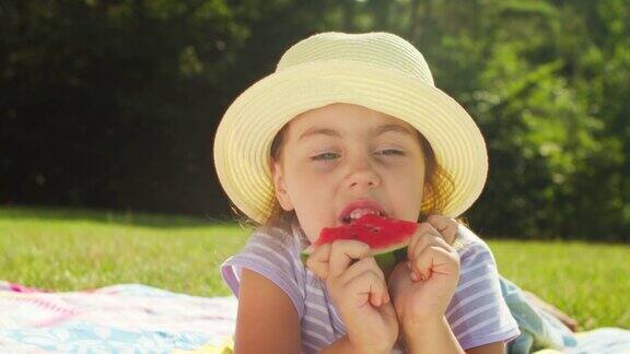 一个阳光明媚的夏日一个可爱的小女孩正躺在森林空地的草地上吃着一个多汁的西瓜