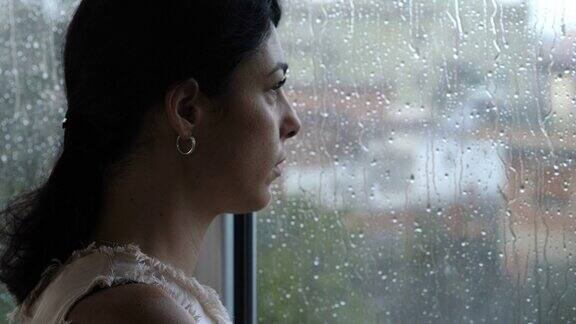 悲伤、沮丧一个下雨天的年轻女子望着窗外