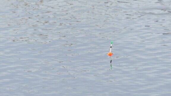 一个红色和绿色的钓鱼浮子在波浪上摆动的特写同时在河上用鱼竿钓鱼