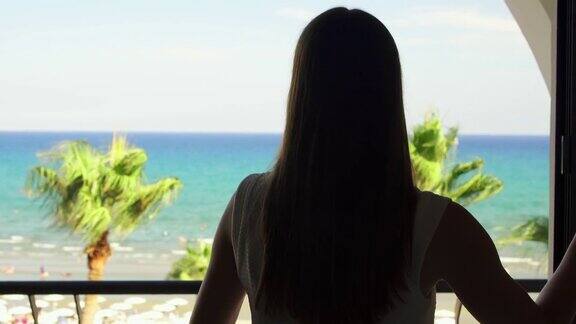 度假的女人打开百叶窗到阳台上欣赏地中海的海景