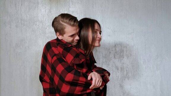 一对年轻美丽的夫妇男人和女人在房子灰色的墙上温柔地拥抱着