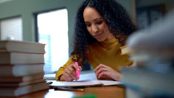 年轻的大学生坐在书桌前用荧光笔在笔记本上写字女性在家学习时学习并突出信息通读笔记准备期末考试