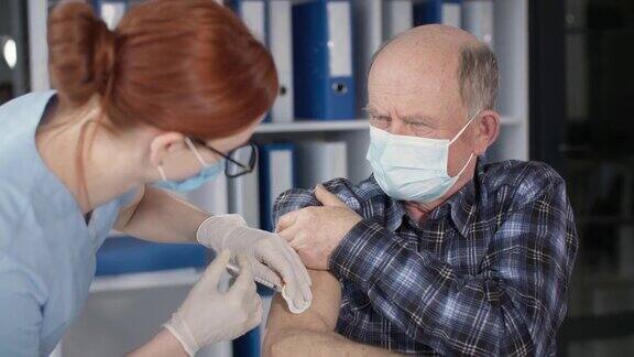 为预防病毒及感染一名戴口罩的老年男性病人在化验室由注射护士注射疫苗