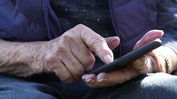 近距离拍摄的老年白人妇女的手使用智能手机的触摸屏户外
