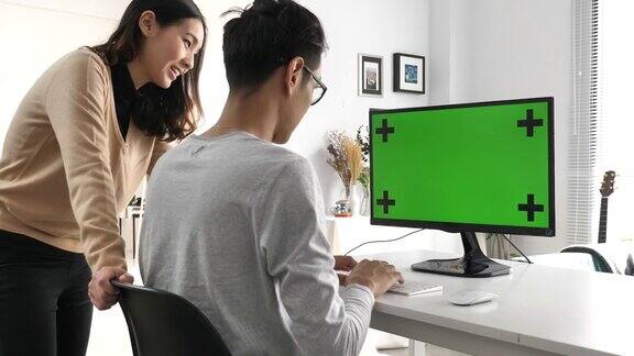 两个亚洲人看着绿色屏幕的电脑
