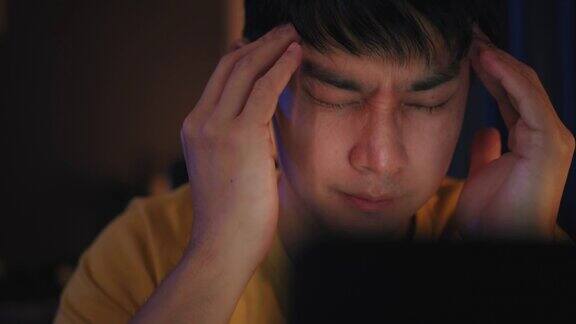 一名亚洲男子在家庭办公室工作到很晚使用笔记本电脑会让他感到昏昏欲睡眼睛会感到压力或抑郁