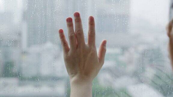 女人的手用雨滴触摸窗户
