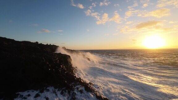 航拍飞行非常近的泡沫浪花海洋撞击岩石海岸由日落岩石