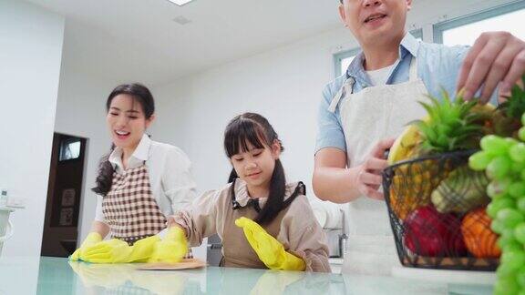 亚洲年轻家庭教他们的女儿清洁厨房柜台孩子和父母一起跳舞一起笑很开心可爱的家庭在快乐的打扫房间时的快乐时刻