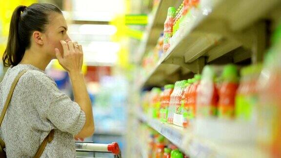 近距离肖像吸引年轻女孩选择果汁在超市附近的货架