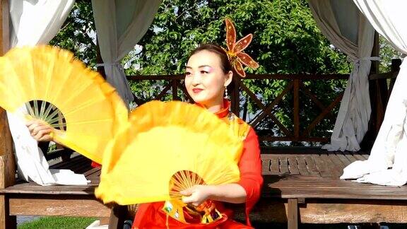 美丽的亚洲女人穿着红色的传统中国服装和两个大的黄色扇子跳舞