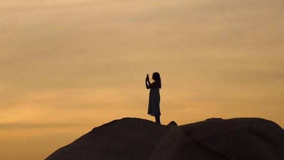 女孩的剪影站在岩石上等待日落