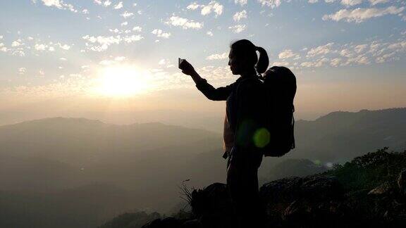 一位女性徒步旅行者用手机拍下了山上日落的照片