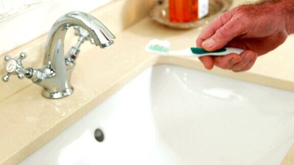 一个老人在浴室里把牙膏放到牙刷上