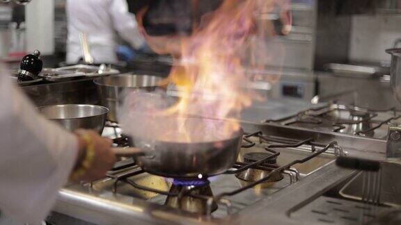厨师在平底锅中烹饪火焰看起来专注专业厨师烹饪火焰风格厨师在商业厨房的燃气灶上煎炸混合食物商业厨房油锅中的慢动作火焰专业厨师在燃气炉上的平底锅中燃烧