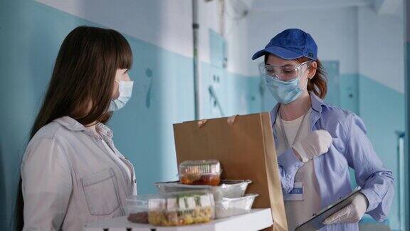 在隔离期间戴着医用口罩的年轻女孩通过戴着口罩和手套的女快递员订购食物