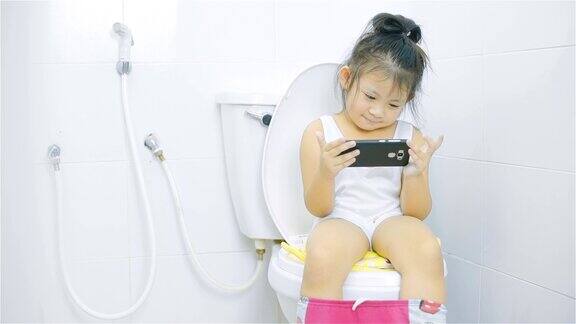 看智能手机的小女孩坐在厕所的马桶上