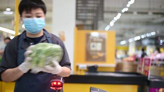 一位亚洲华人女性超市零售店员收银员在柜台结账时扫描蔬菜的价格