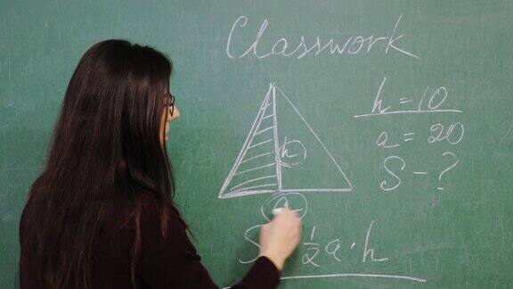 在线教育女老师正在进行在线数学课在学校上课时她正在黑板上用粉笔写规则、公式远程教学封锁学校