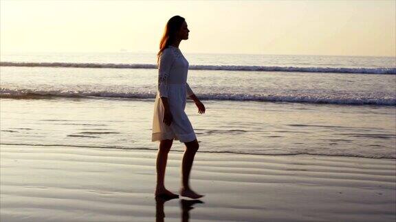 慢动作的女人赤脚走在潮湿的海边在日落