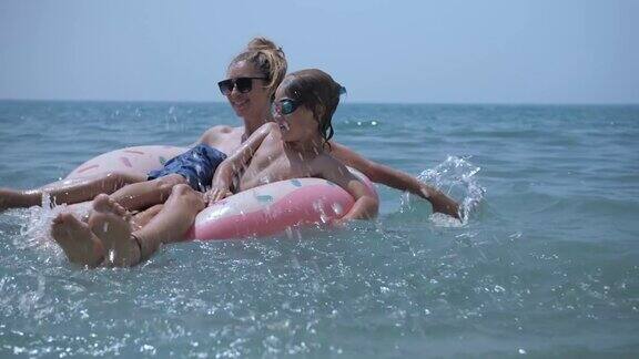 一家人在充气玩具甜甜圈上放松在蓝色的大海里游泳