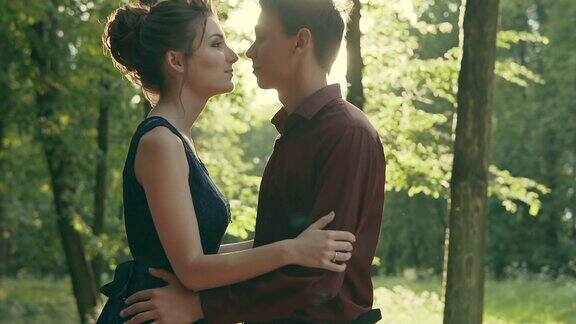 浪漫的年轻夫妇拥抱在公园日落的灯光背景