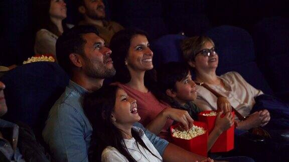 幸福的家庭在电影院看一部有趣的电影一边吃着爆米花和苏打水