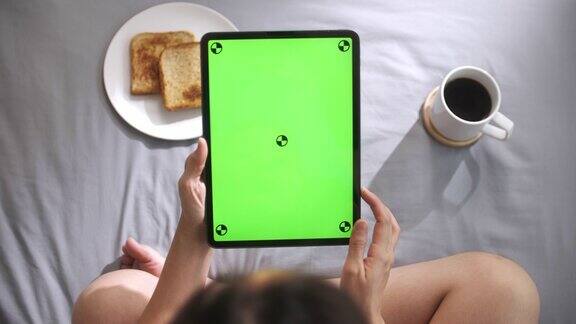 早上在床上用绿色屏幕看数字平板电脑的女人垂直