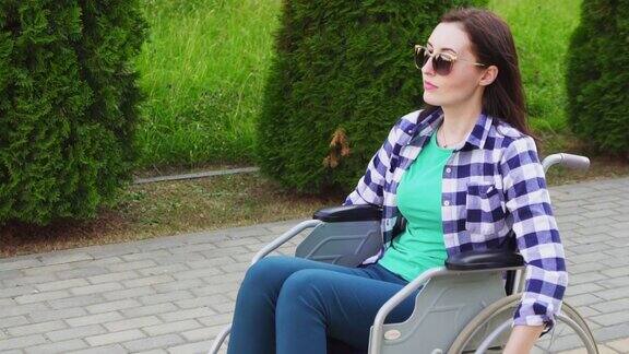迷人的残疾女孩穿着衬衫和眼镜坐在轮椅上在公园里慢悠悠地走着